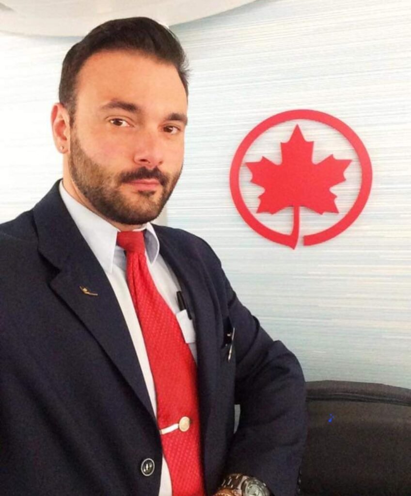 Michael in his flight attendant uniform standing next to an Air Canada logo.